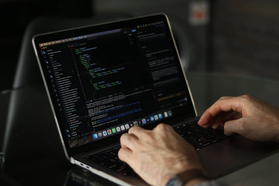 A close-up photograph of a laptop computer on a wooden desk, displaying lines of programming code with syntax highlighting on its screen. To the right of the laptop, there is a ceramic coffee mug with